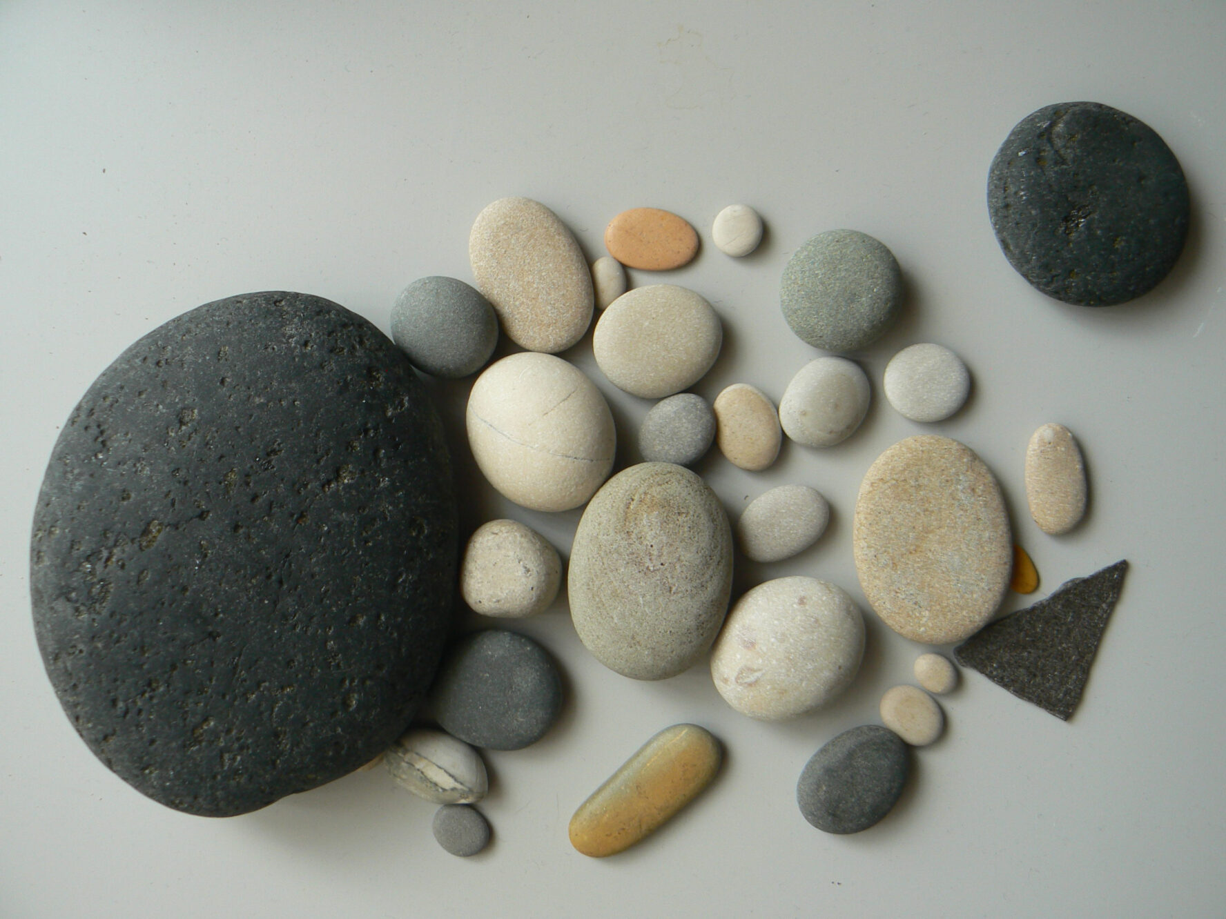 Kieselsteine in verschiedenen Farben und Größen liegen auf einem hellgrauen Untergrund.